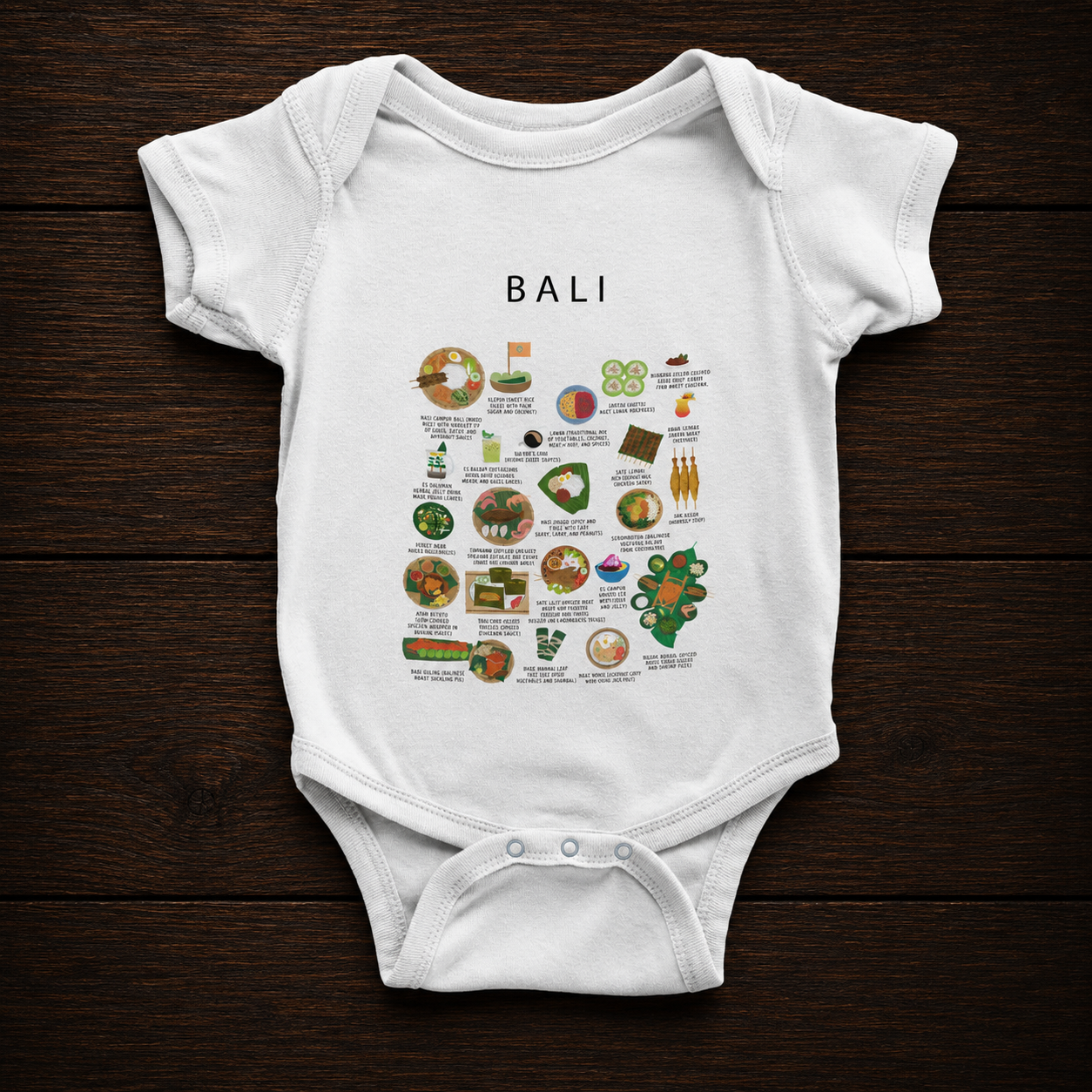 White Bali food baby onesie flat-lay on dark wood grain