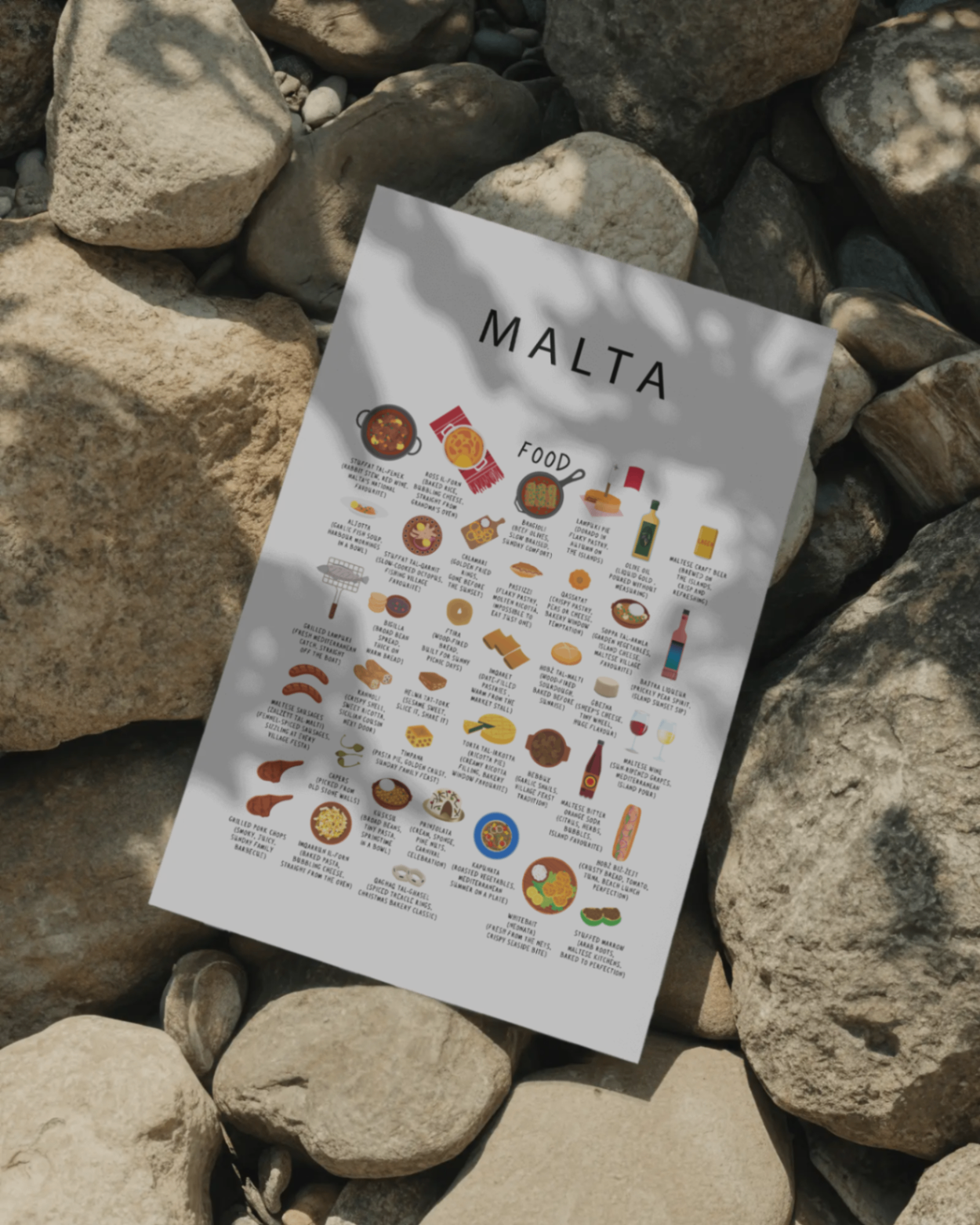 White Malta food poster resting on smooth Mediterranean stones in golden sunlight