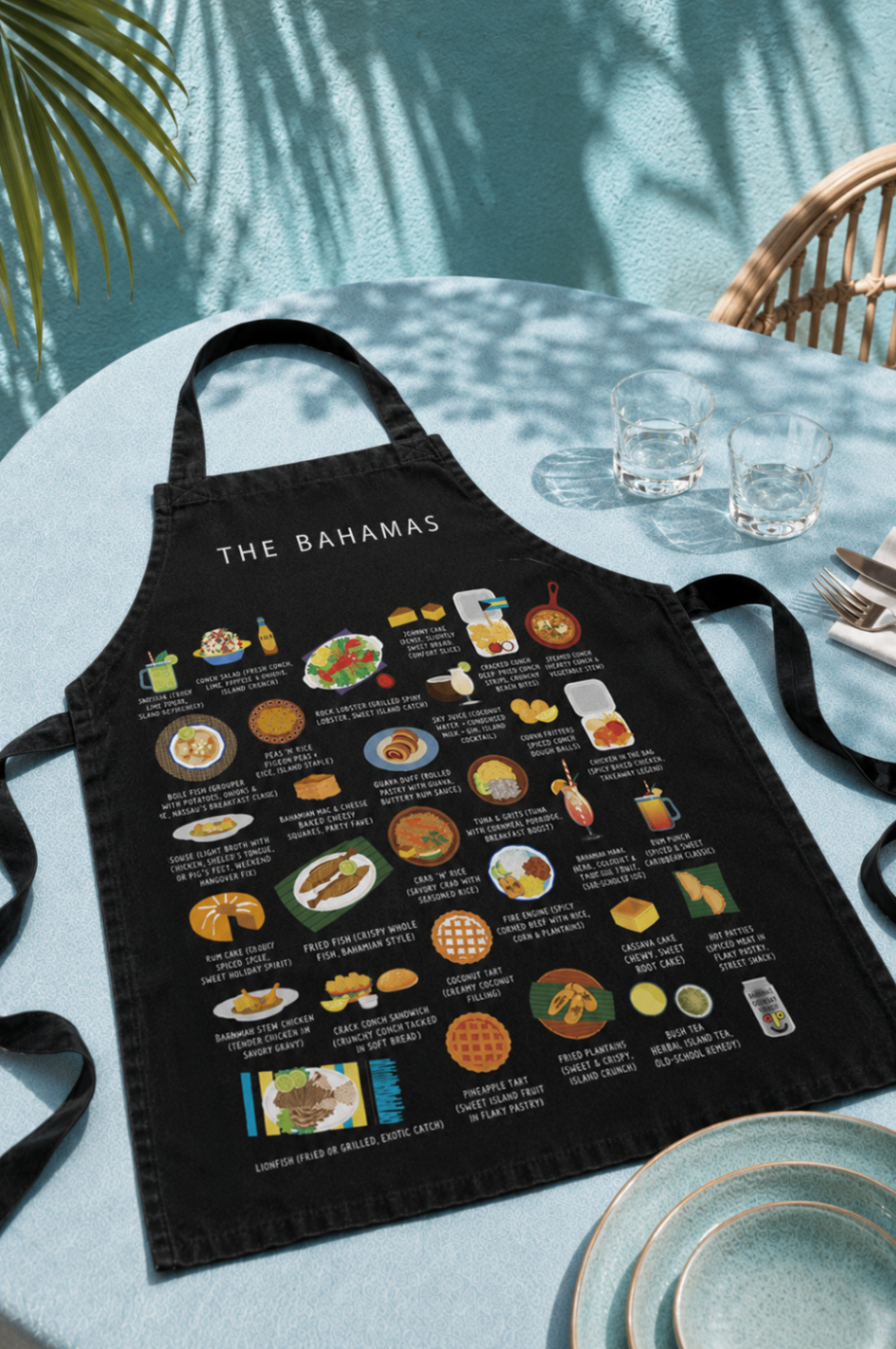 Black Bahamas food apron styled on a poolside table with palm shadows and cocktail glasses
