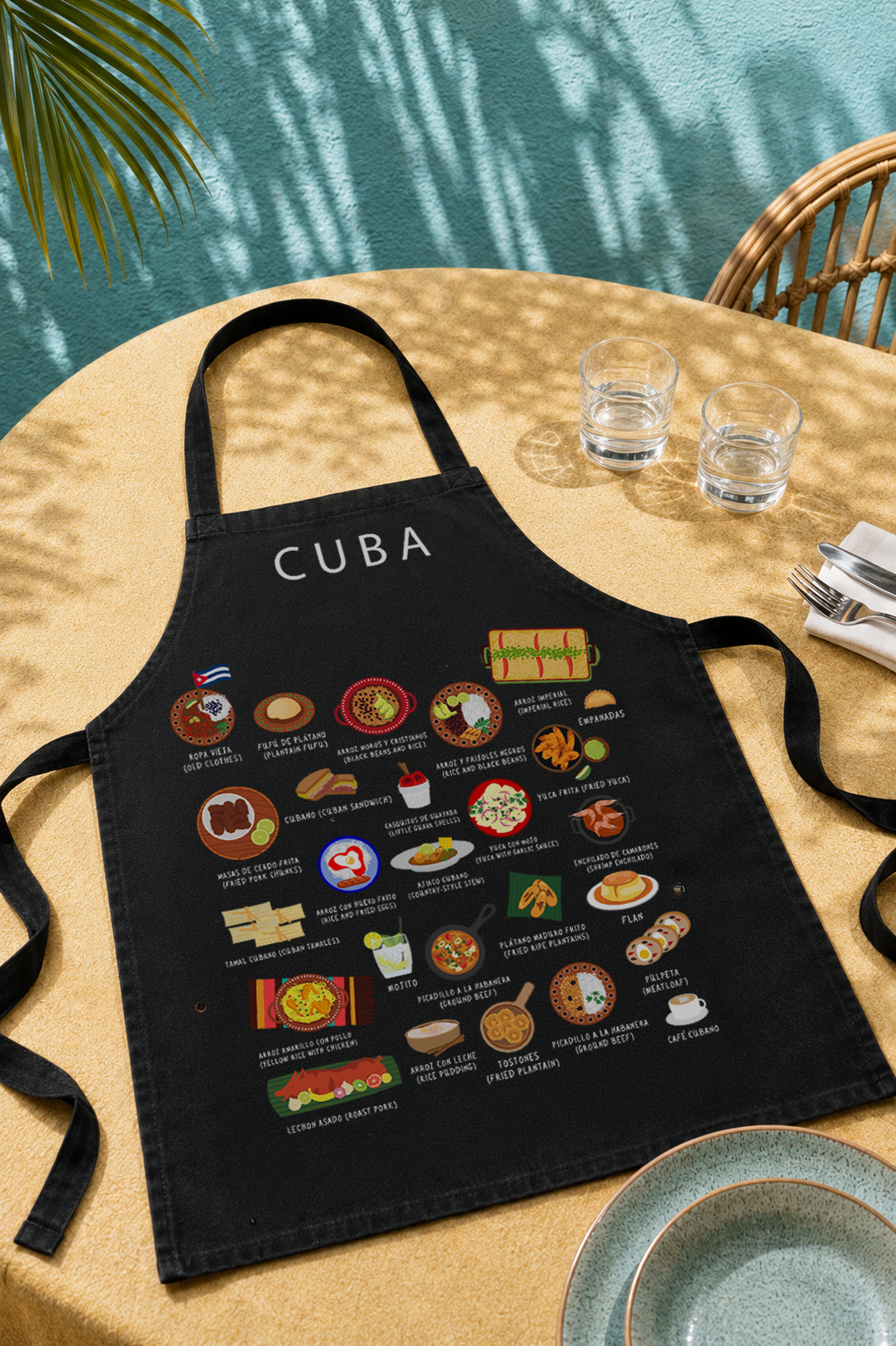 Black Cuba food apron laid on a sunlit outdoor table with turquoise wall and palm shadow