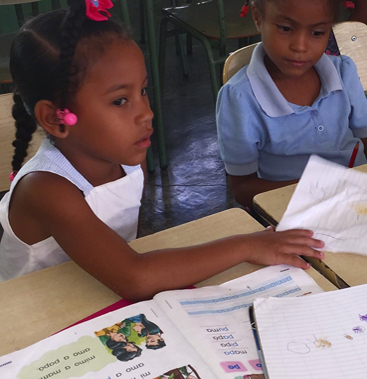 Young students reading illustrated books at their desks in a school in the Dominican Republic that received a donated Maps By Annie map.