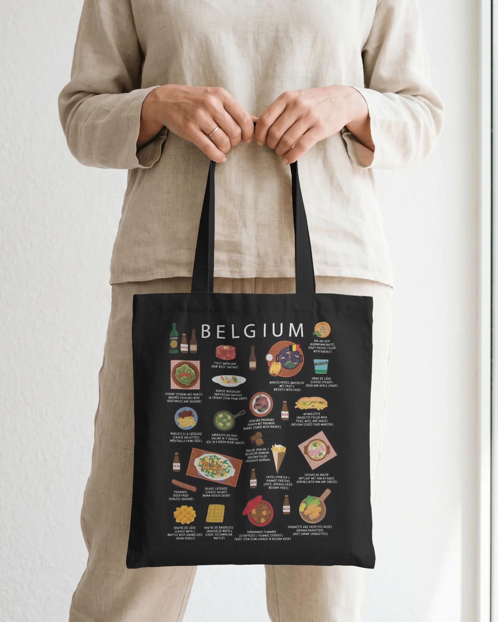 Black Belgium food tote bag held in soft daylight against a neutral linen outfit