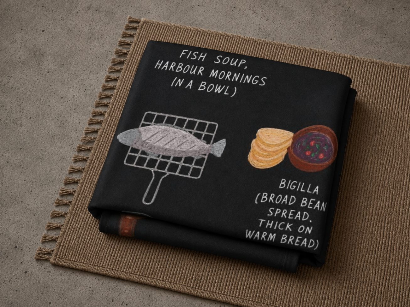Folded Malta food blanket resting on a woven mat with warm daylight