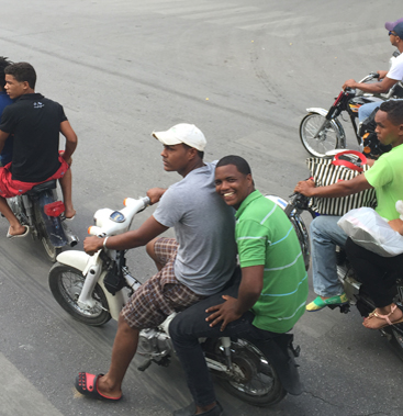 A busy street scene captured on an early Maison Maps travel journey, families riding through a Caribbean town.