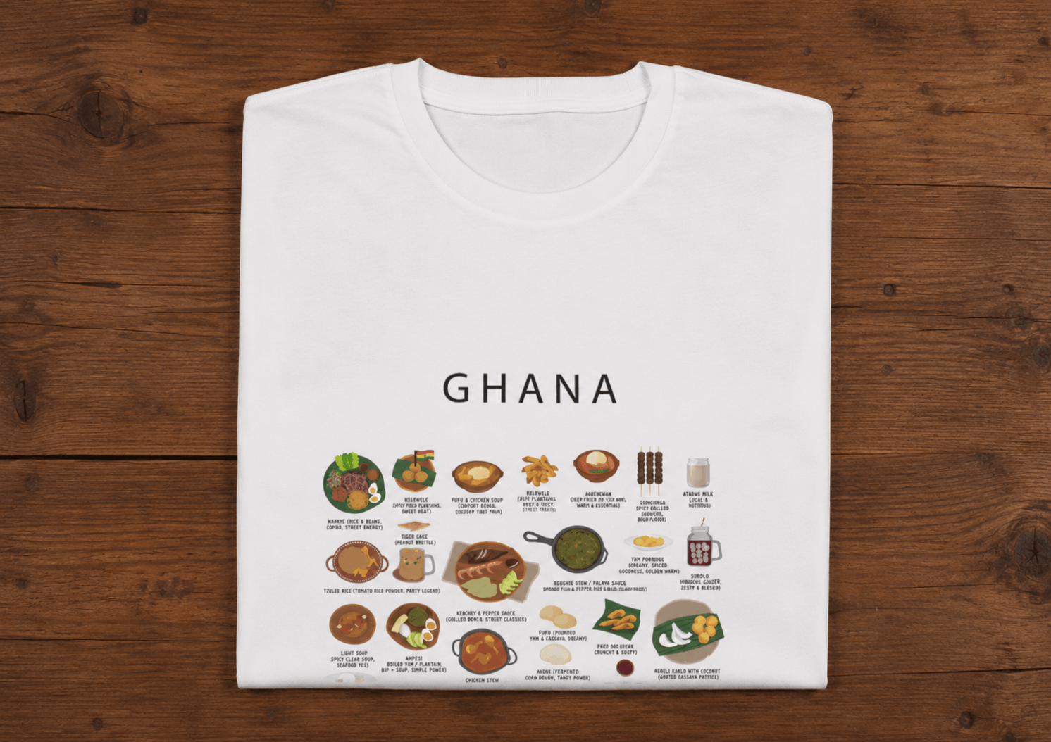 White Ghana food t-shirt folded on a dark wooden surface with jollof, kelewele and waakye illustrations