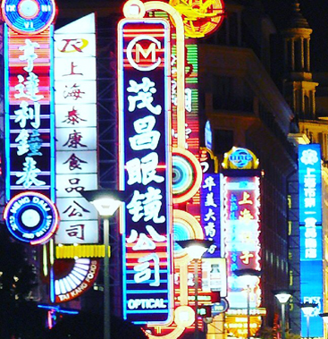 Neon signs in Chinese characters lighting up Nanjing Road in Shanghai at night, glowing in red, blue, and yellow above the shopping street.