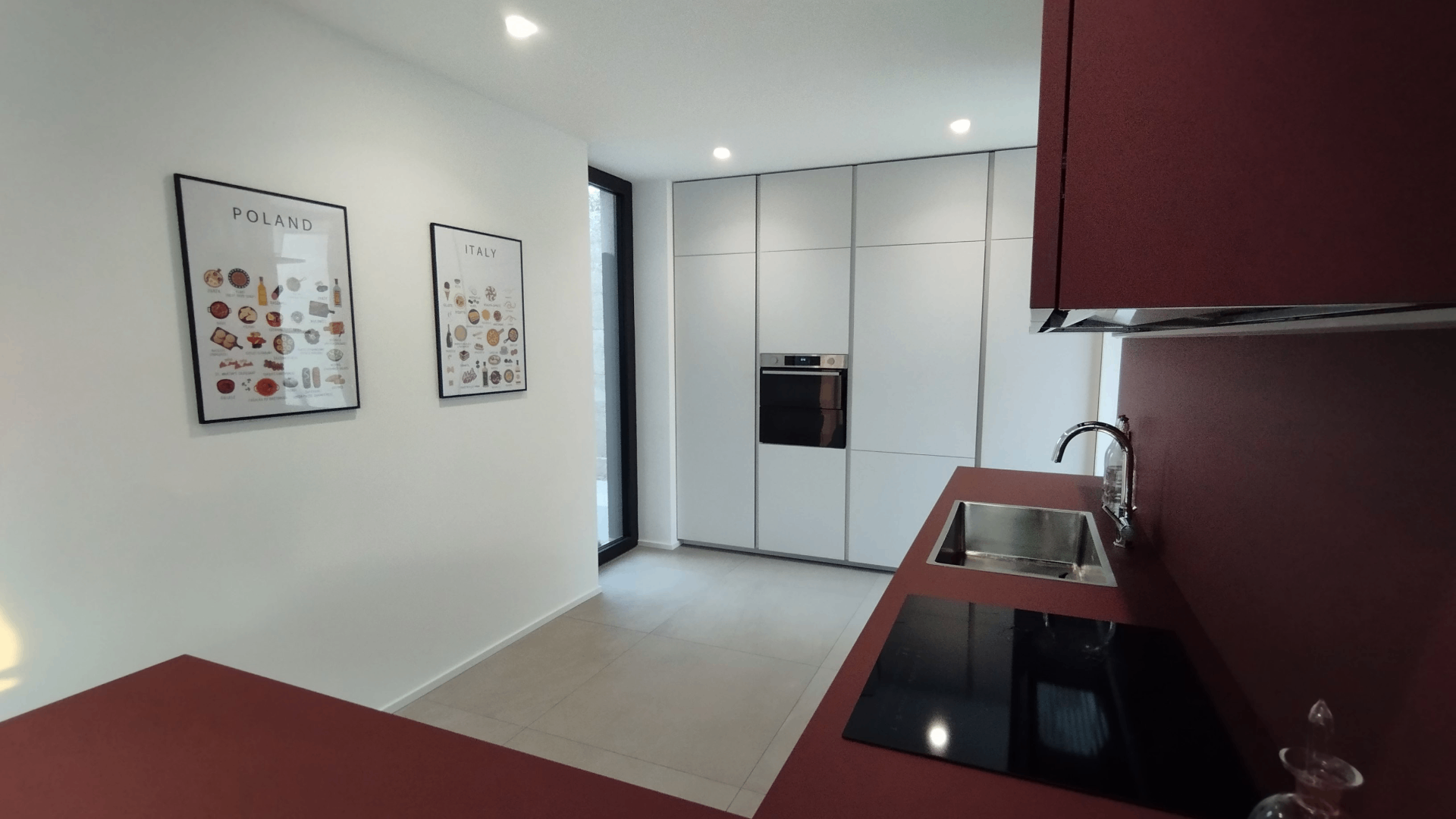 Interior of Madema Studio in Udine, Italy, with framed Maison Maps Poland and Italy food posters on a white wall beside a minimalist kitchen.