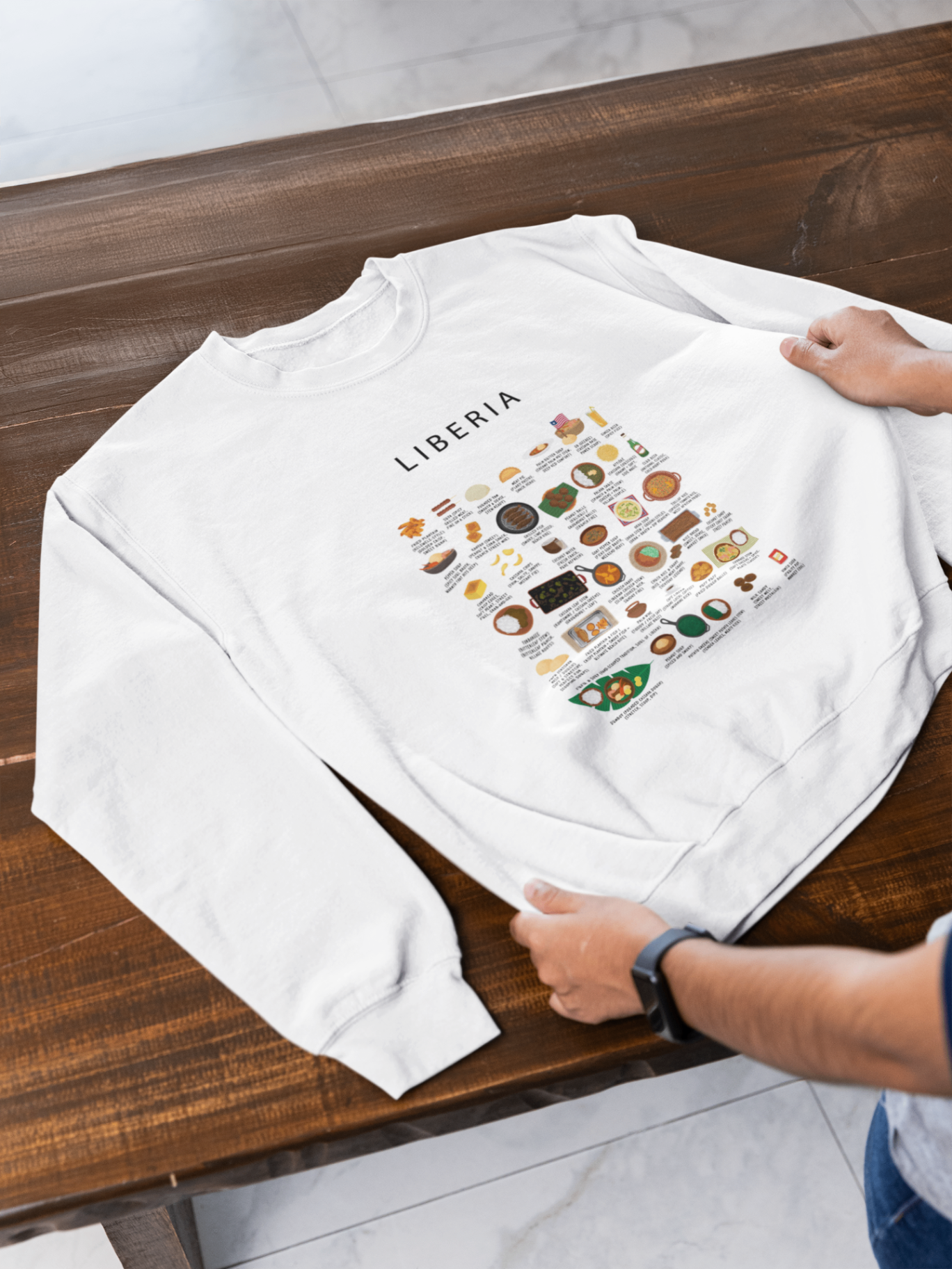 White Liberia food sweatshirt held on a dark wooden bench in soft daylight