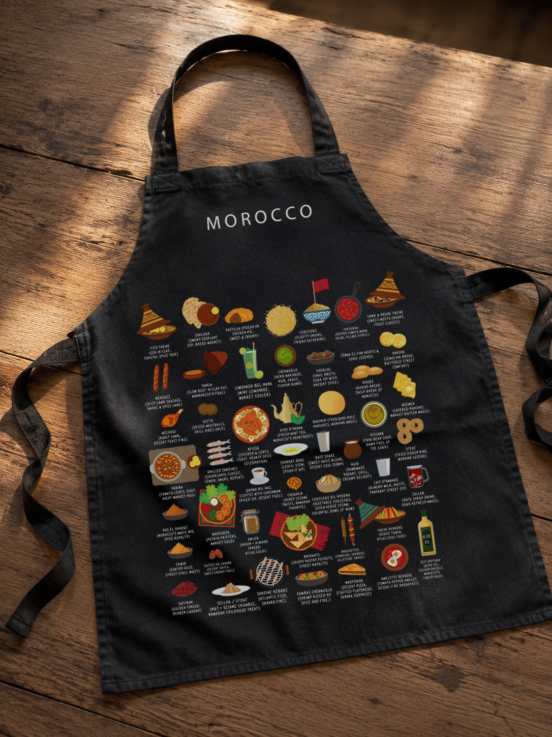 Black Morocco food apron laid across a rustic wooden table in warm golden light