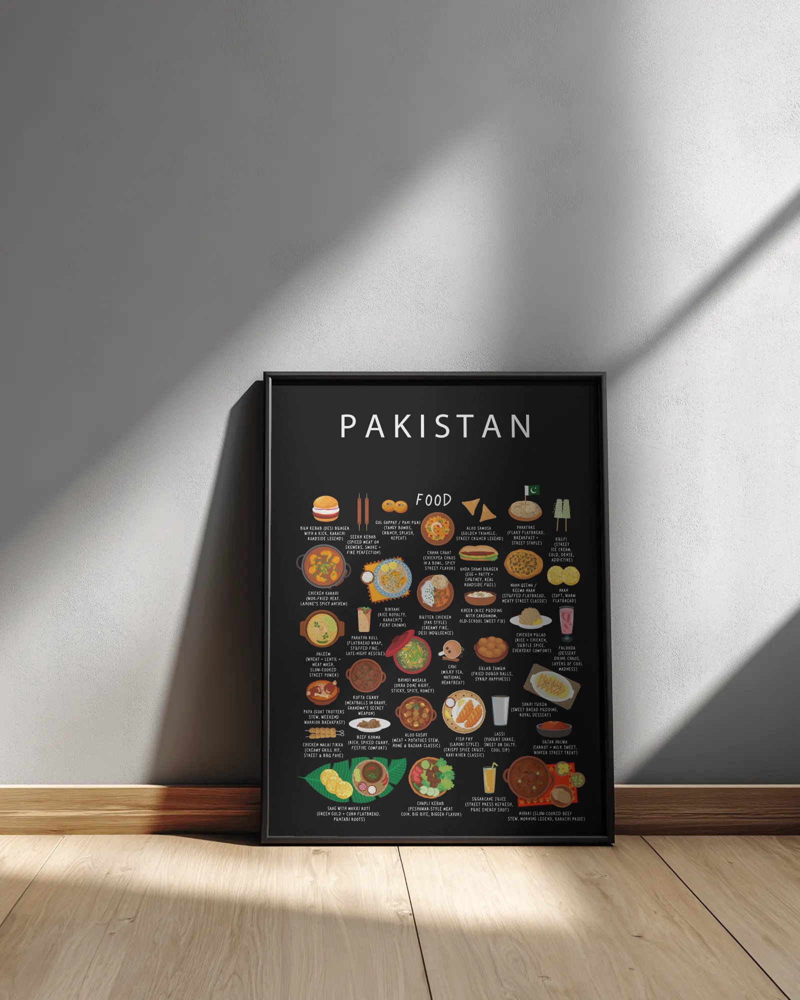 Framed black Pakistan food poster resting against a pale wall in diagonal sunlight