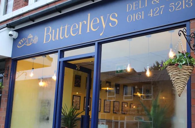 Deep blue exterior of Butterleys Deli and Café in Marple, United Kingdom, with framed Maison Maps food posters visible through the window.