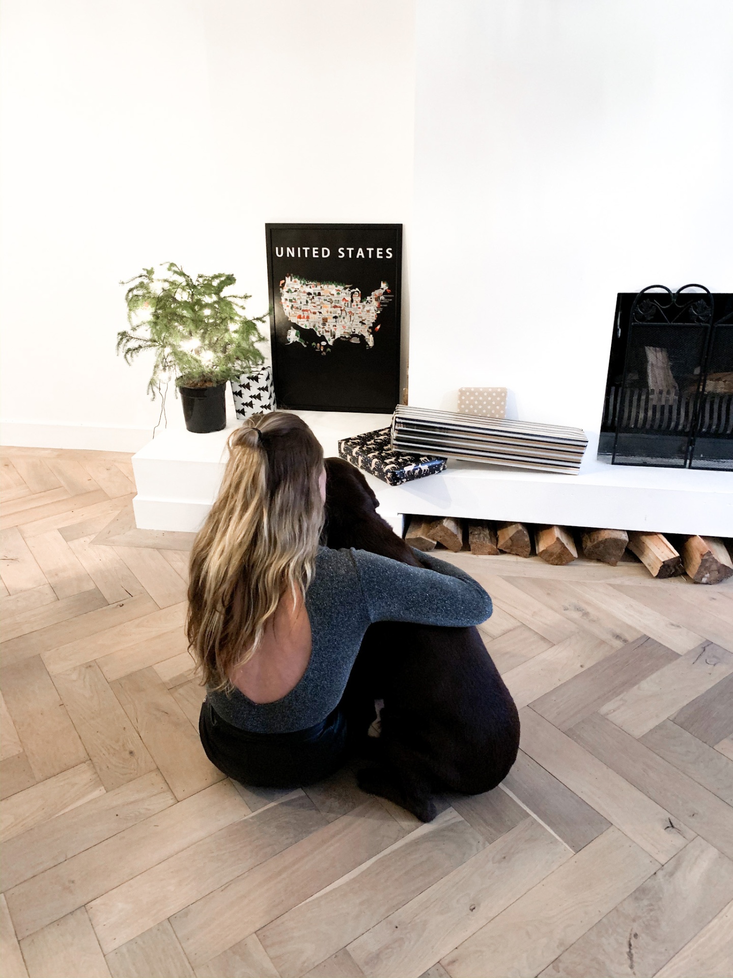 Anneke, founder of Maison Maps, sitting on a herringbone wooden floor with her black Labrador in front of a framed Maison Maps United States poster.
