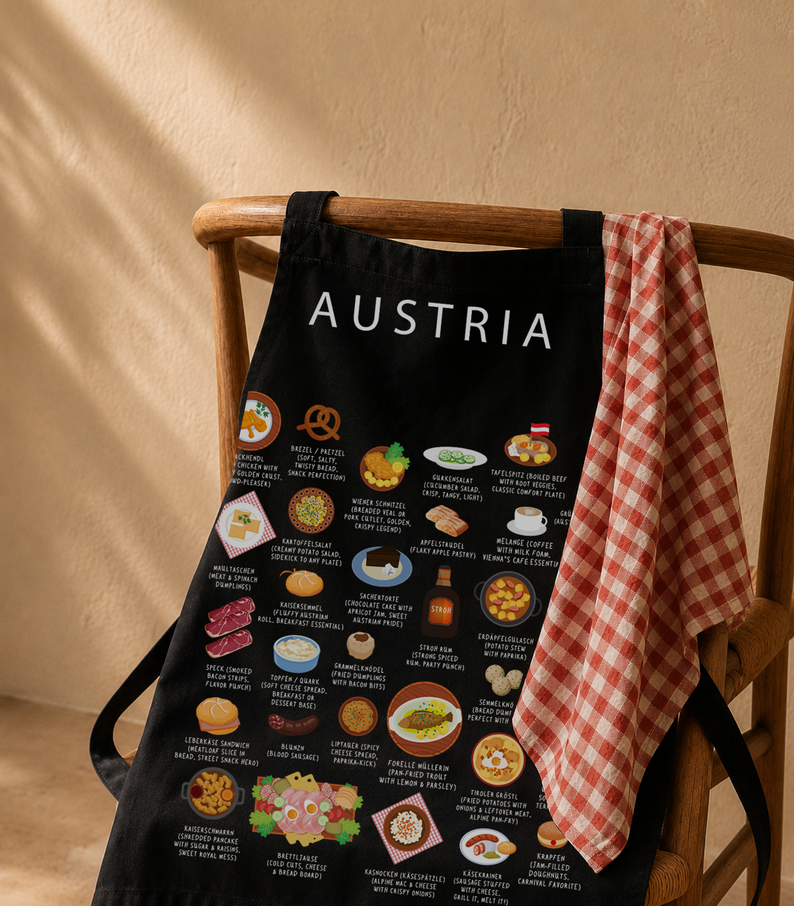 Black Austria food apron draped over a wooden chair beside a red gingham cloth in warm daylight