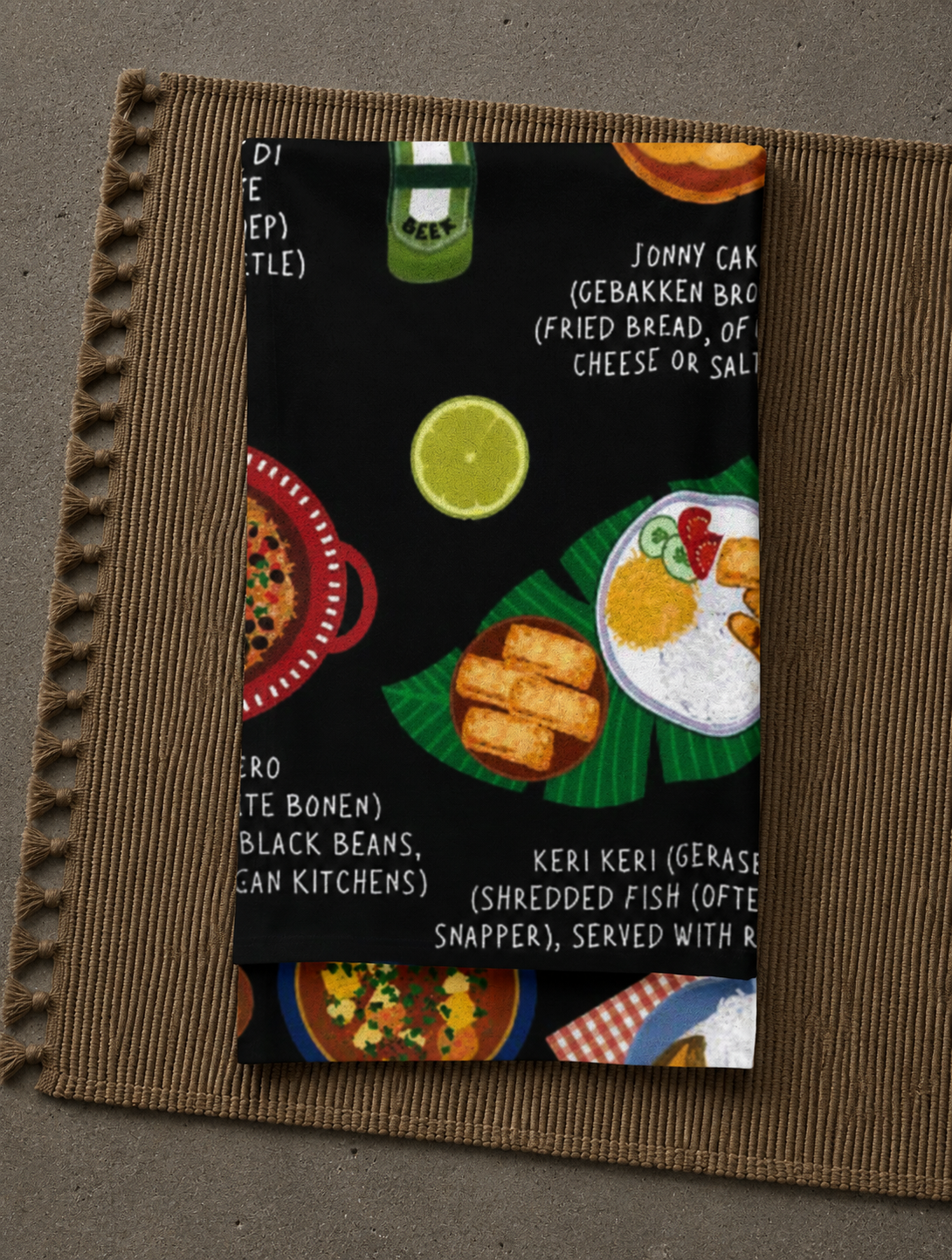 Black Aruba food blanket folded on a woven placemat with tassel trim