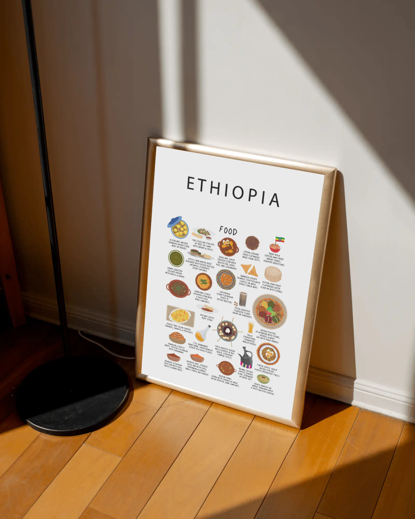 White Ethiopia food poster in a warm gold frame leaning against a sunlit wall on a wooden floor