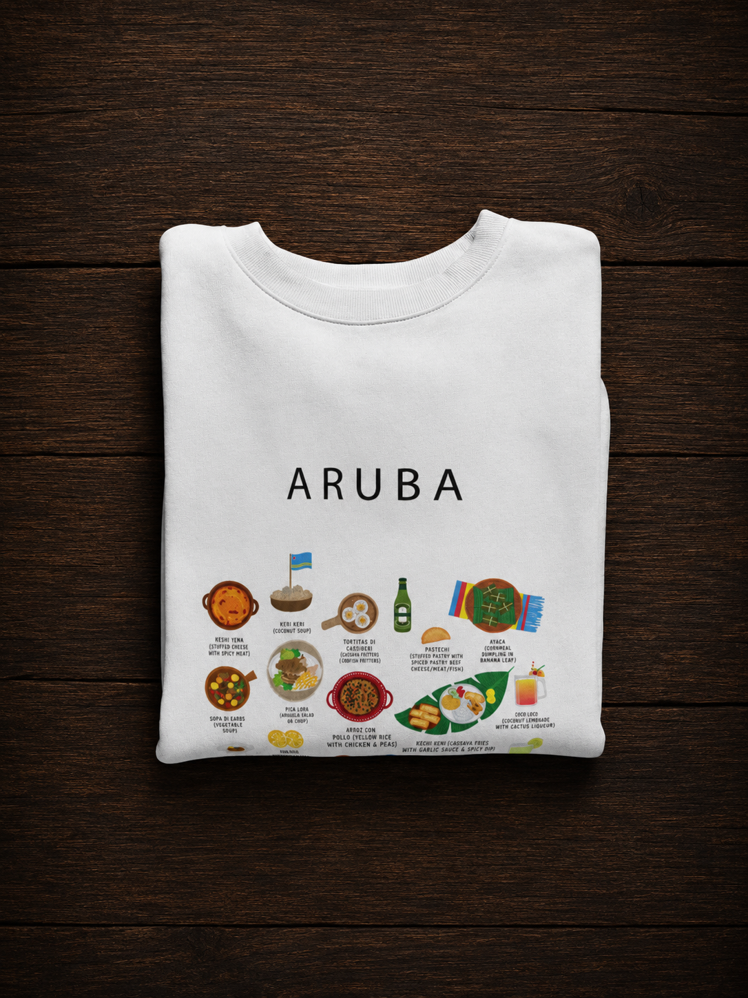 White Aruba food sweatshirt folded on a dark wooden surface in warm directional light