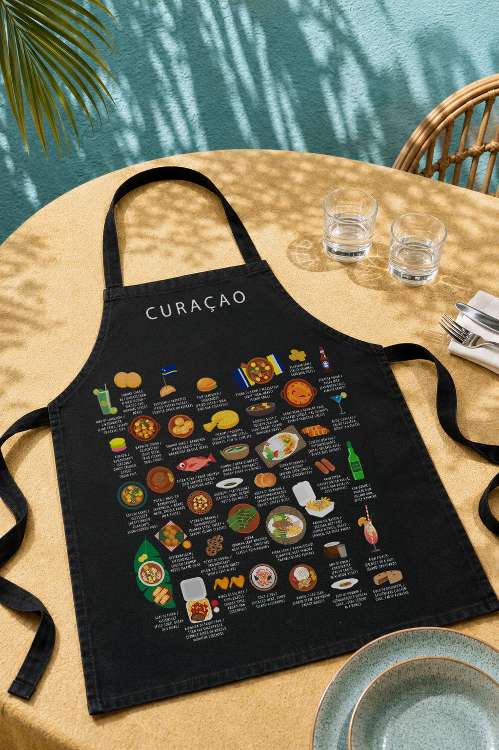 Black Curaçao food apron on a sunlit outdoor table with turquoise wall, palm shadow and water glasses