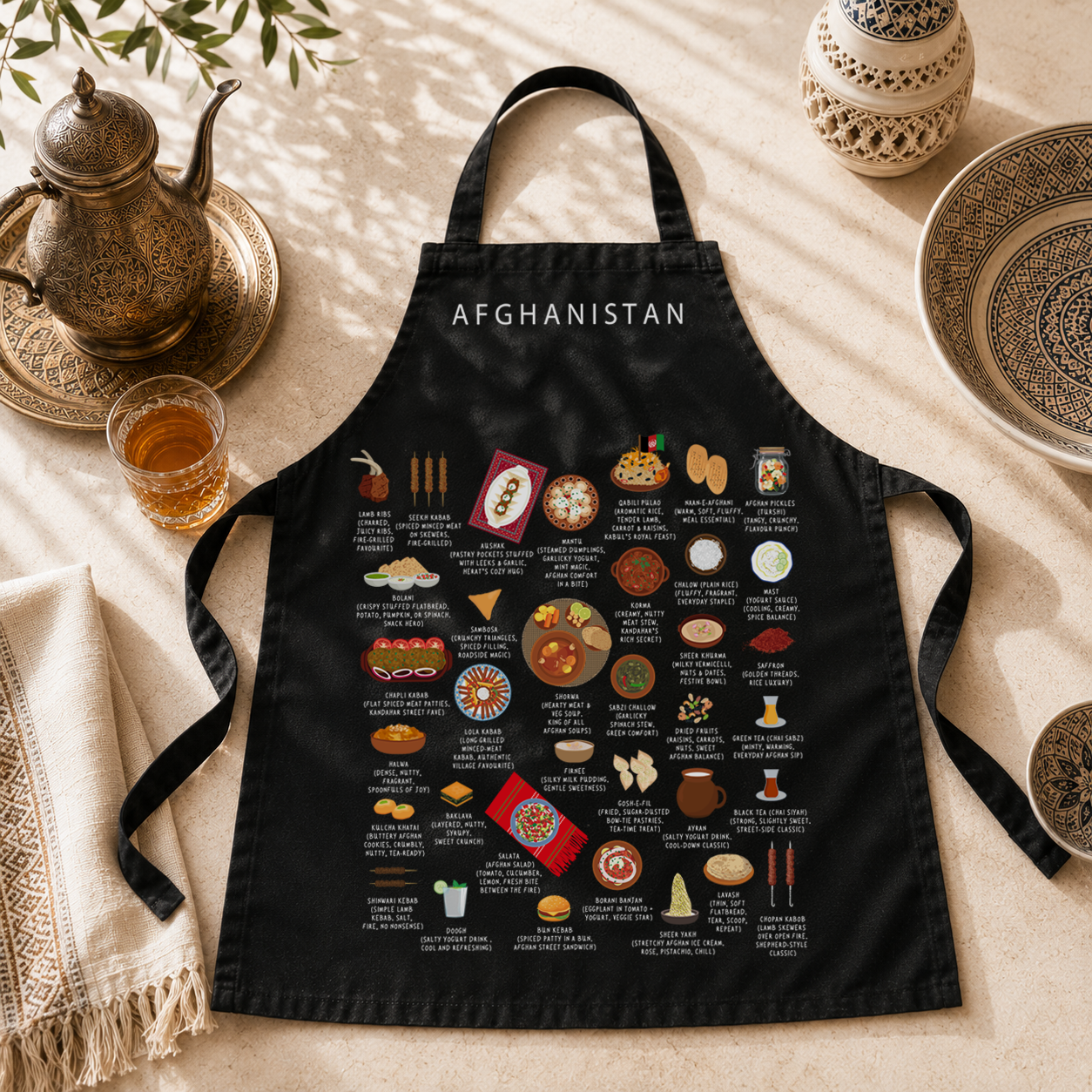 Black Afghanistan food apron styled on a sunlit table with brass teapot and Afghan ceramics