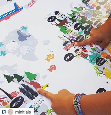 Close-up of two children's hands adding colourful character and speech-bubble stickers to the Maison Maps illustrated world map on a table.